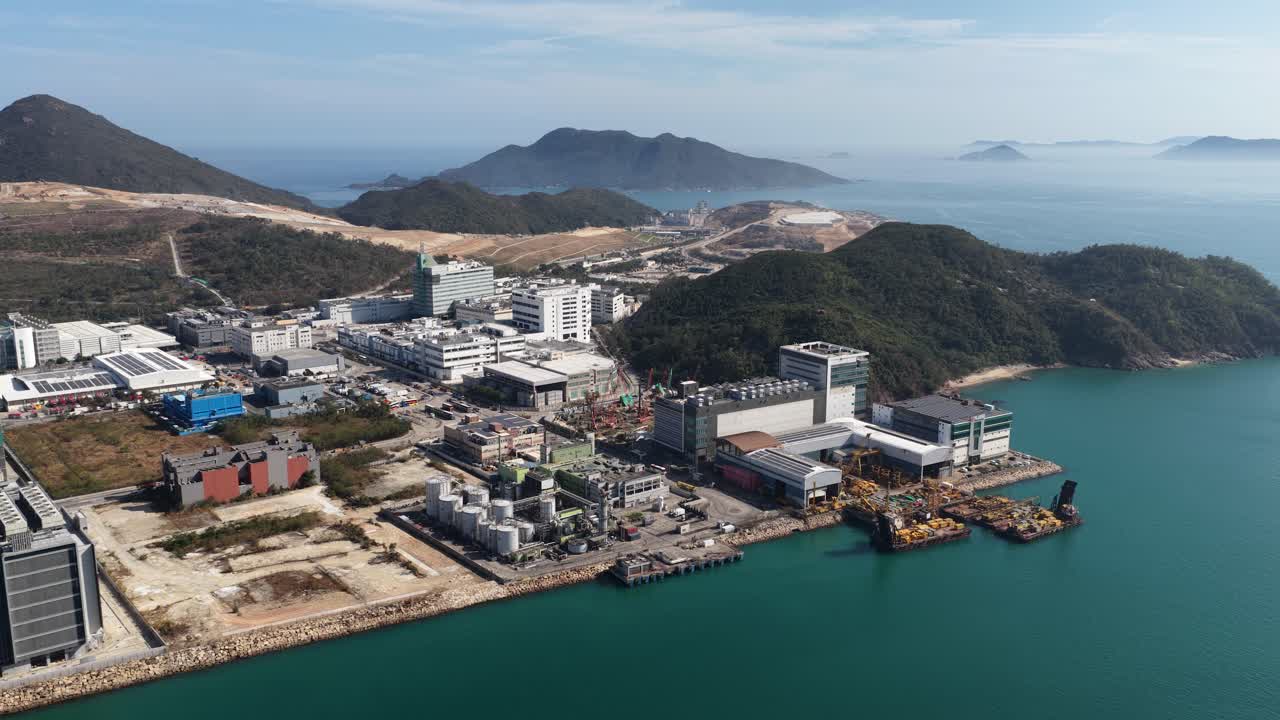 Toàn cảnh từ trên cao tuyệt đẹp của khu công nghiệp Tseung Kwan O giữa những ngọn đồi xanh và biển xanh ngọc, thể hiện cơ sở hạ tầng ven biển hiện đại, các khu công nghiệp và sự phát triển ven biển