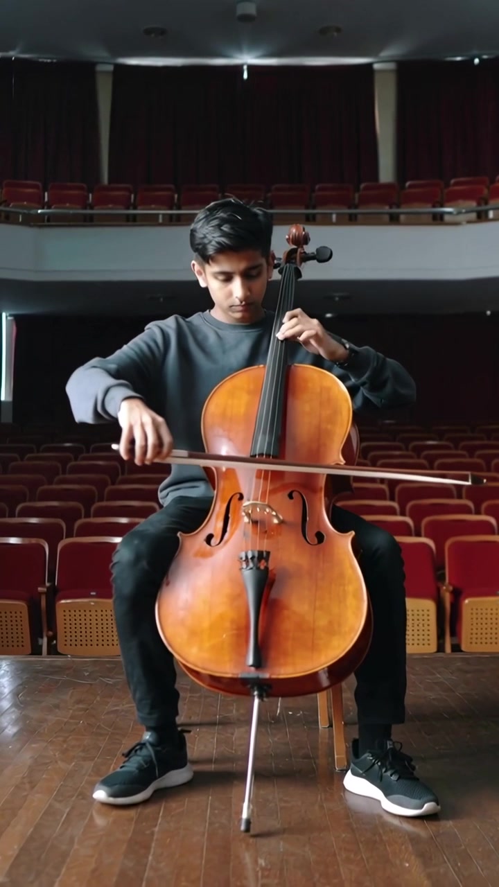 Vertical video: Playing teen cellist in grey top practicing on stage with cello and empty seats