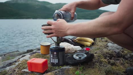 camper preparing to cook outdoor by the lake shore with camping gas stove