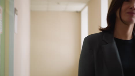 confident businesswoman in gray suit walks toward camera in bright office hallway with composed expression, portraying determination, authority, and calm focus in corporate professional environment