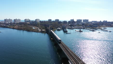 An-aerial-shot-of-a-train-crossing-over-the-bay-in-Queens,-NY