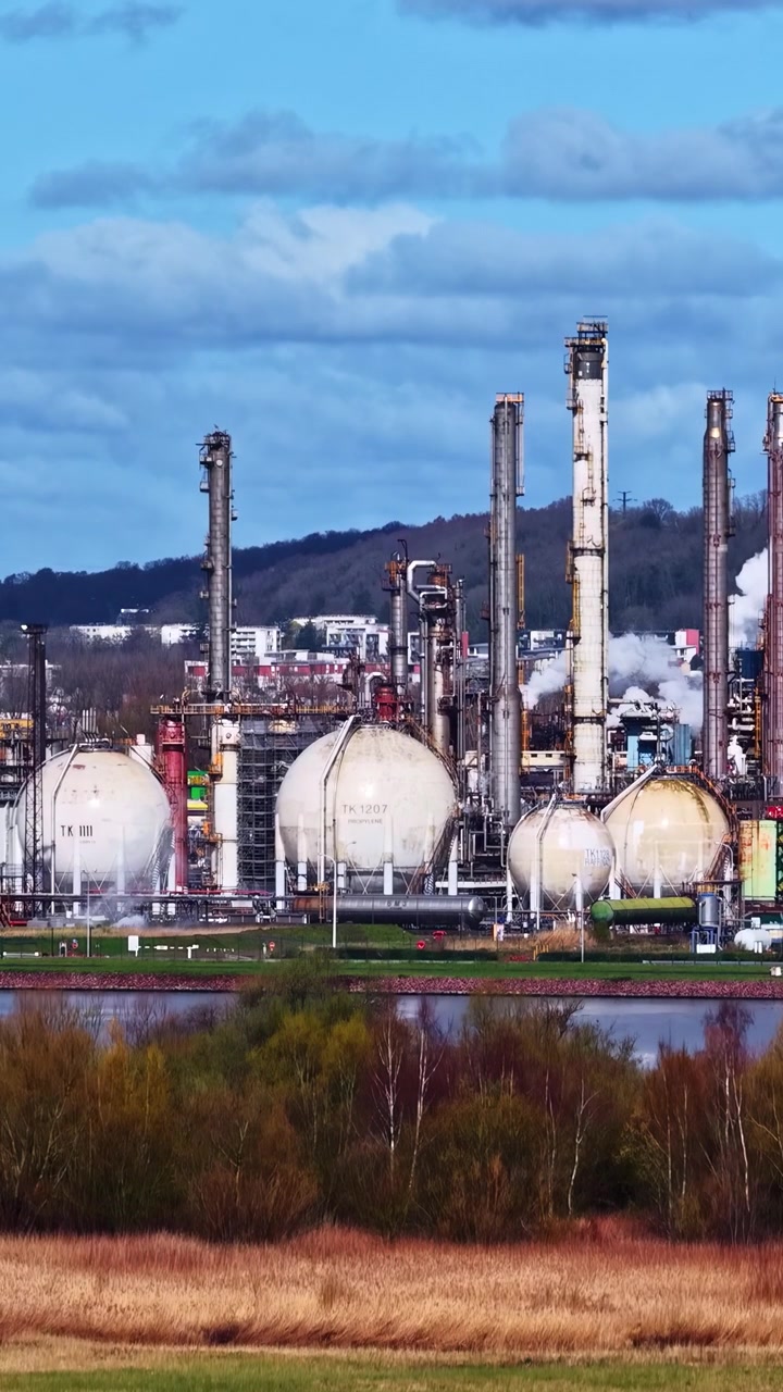 Una extensa instalación industrial con tanques de almacenamiento esféricos y altas chimeneas cerca de un río. Ideal para ilustrar paisajes industriales o temas medioambientales