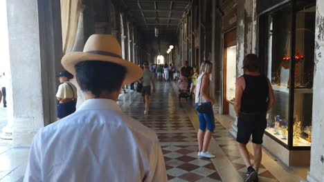 venice, man walking with a hat under san marco square arcade, cinematographic, daytime, 6 seconds, hd, 30 frames per second