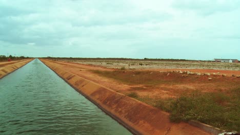 Todavía-La-Vista-De-Un-Canal-Artificial-En-Una-Zona-Rural-Con-Un-Campo-Estéril-En-El-Fondo