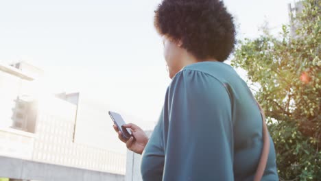 Plus-size-biracial-woman-walking-on-stairs-with-smartphone-in-city