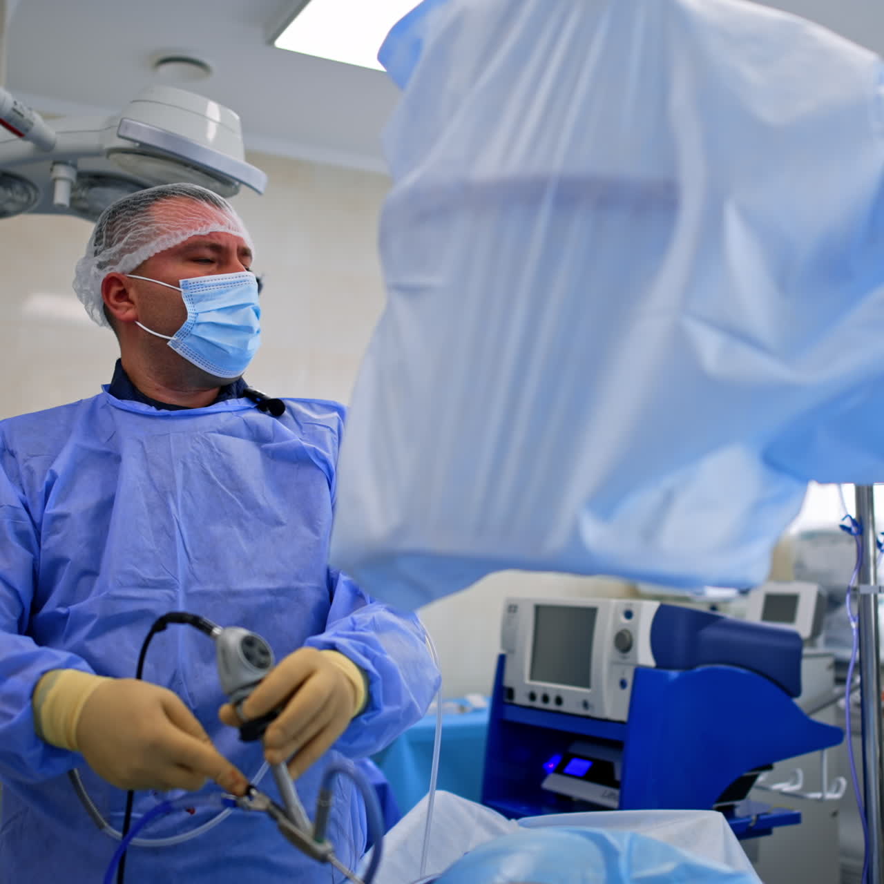 Doctor in mask moves endoscopic device in patient's body. Focused surgeon looking side on the monitor.
