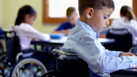 a boy in a wheelchair is sitting at a desk in a classroom