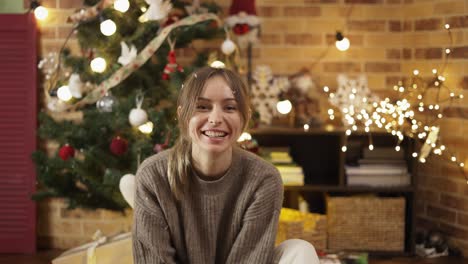 beautiful blonde woman blows snow confetti from hands near christmas tree