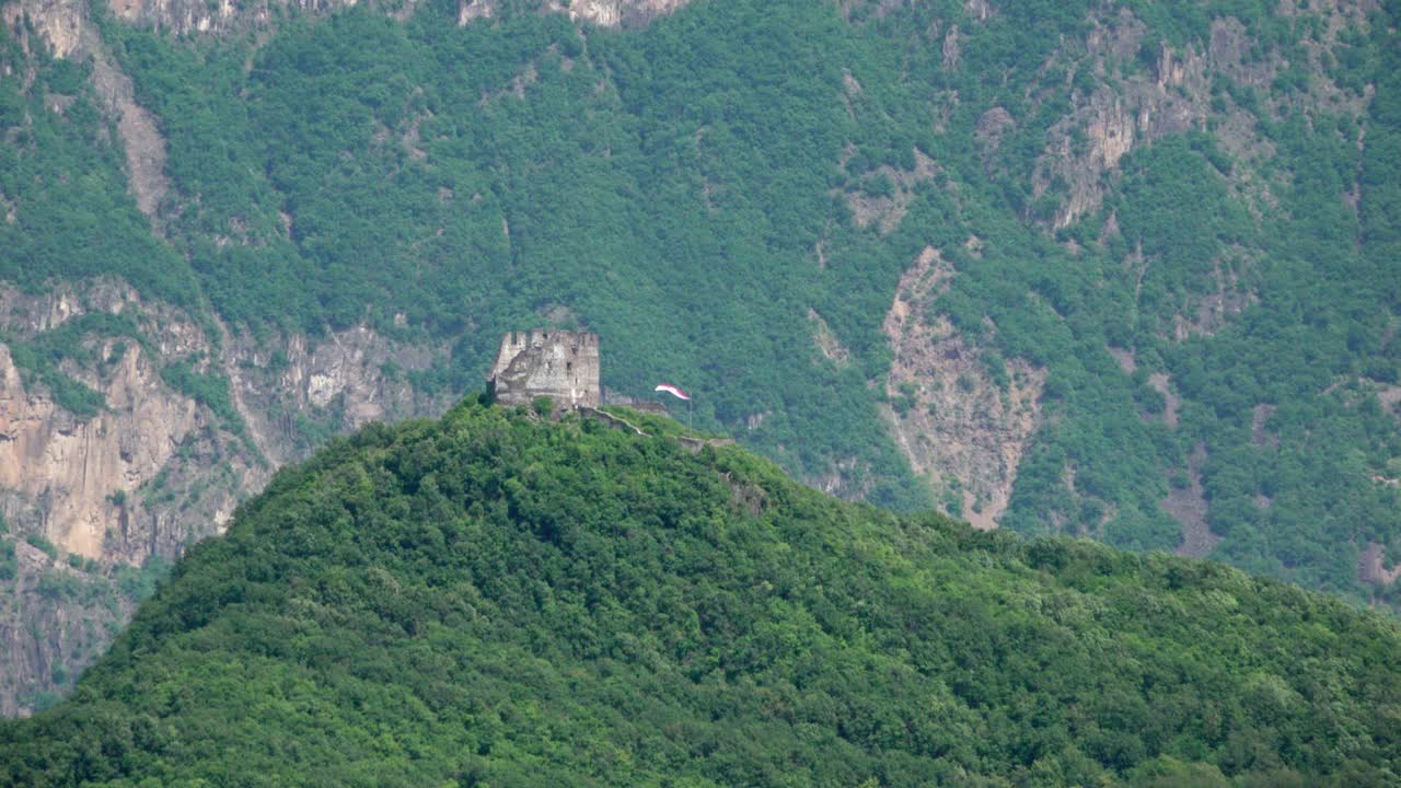 Ruins of Leuchtenburg Castle on a mountaintop with a South Tyrolean flag waving in the wind above Lake Kalterer See, South Tyrol, Italy