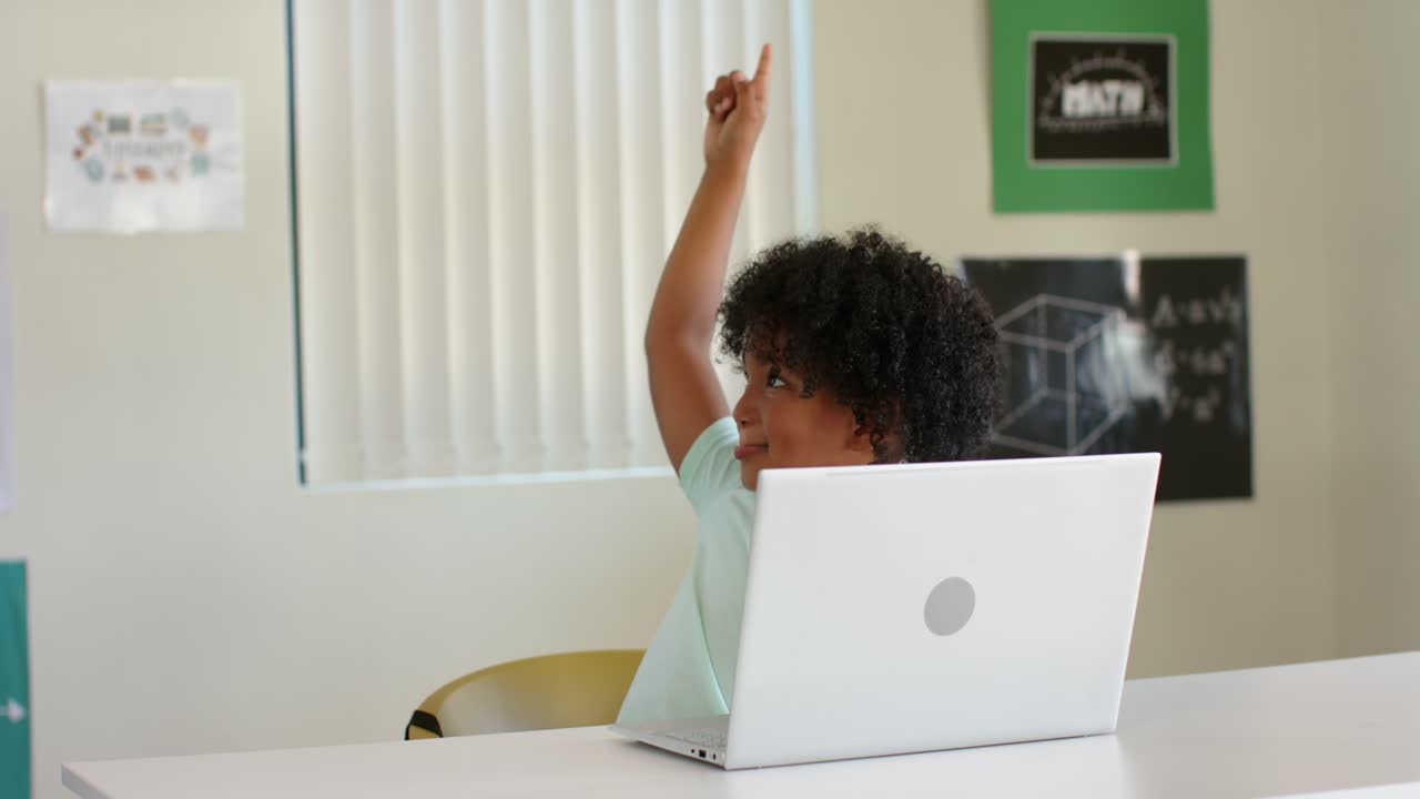 Ragazzo che alza la mano dopo aver guardato a sinistra, cercando aiuto mentre un adulto si china e parla al laptop.