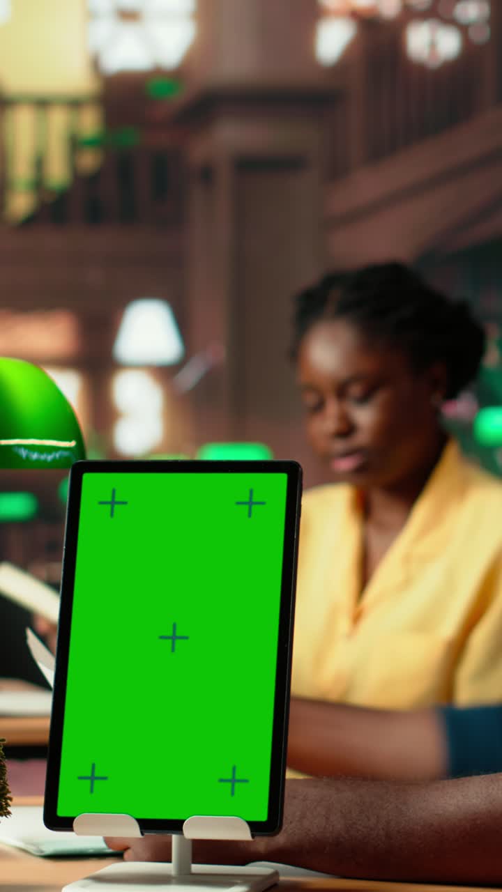 Tablet con schermo verde su scrivania in biblioteca con studenti