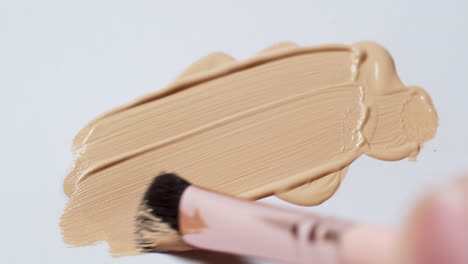 brushing a smudge of nude colored foundation, using a brush applicator on a clean, white paper board