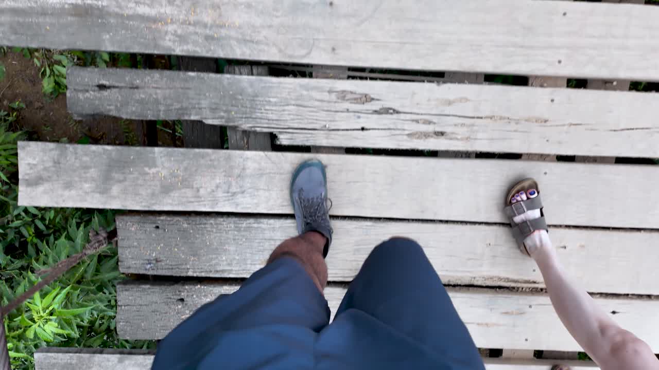 Person walking across a wooden suspension bridge with a first person view