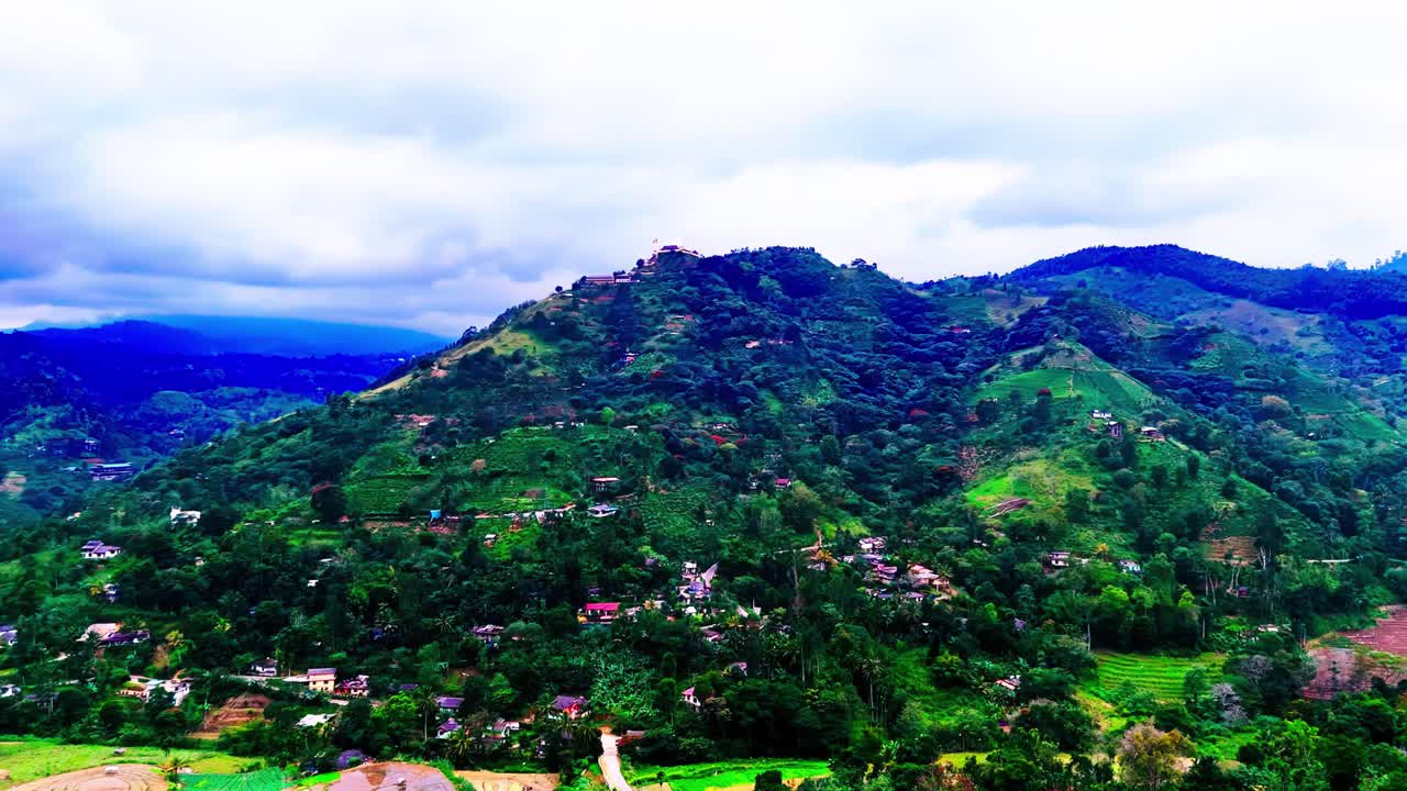 A sweeping view of Sri Lanka’s green mountain slopes dotted with village houses, winding roads, and layered tropical hills under a moody, cloud-filled sky, radiating rural beauty.