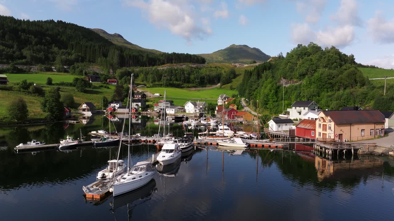 노르웨이의 웅장한 푸른 언덕 아래에서 항구에 정박한 선박들이 조용히 는 동안 공중 드론이 상승합니다.