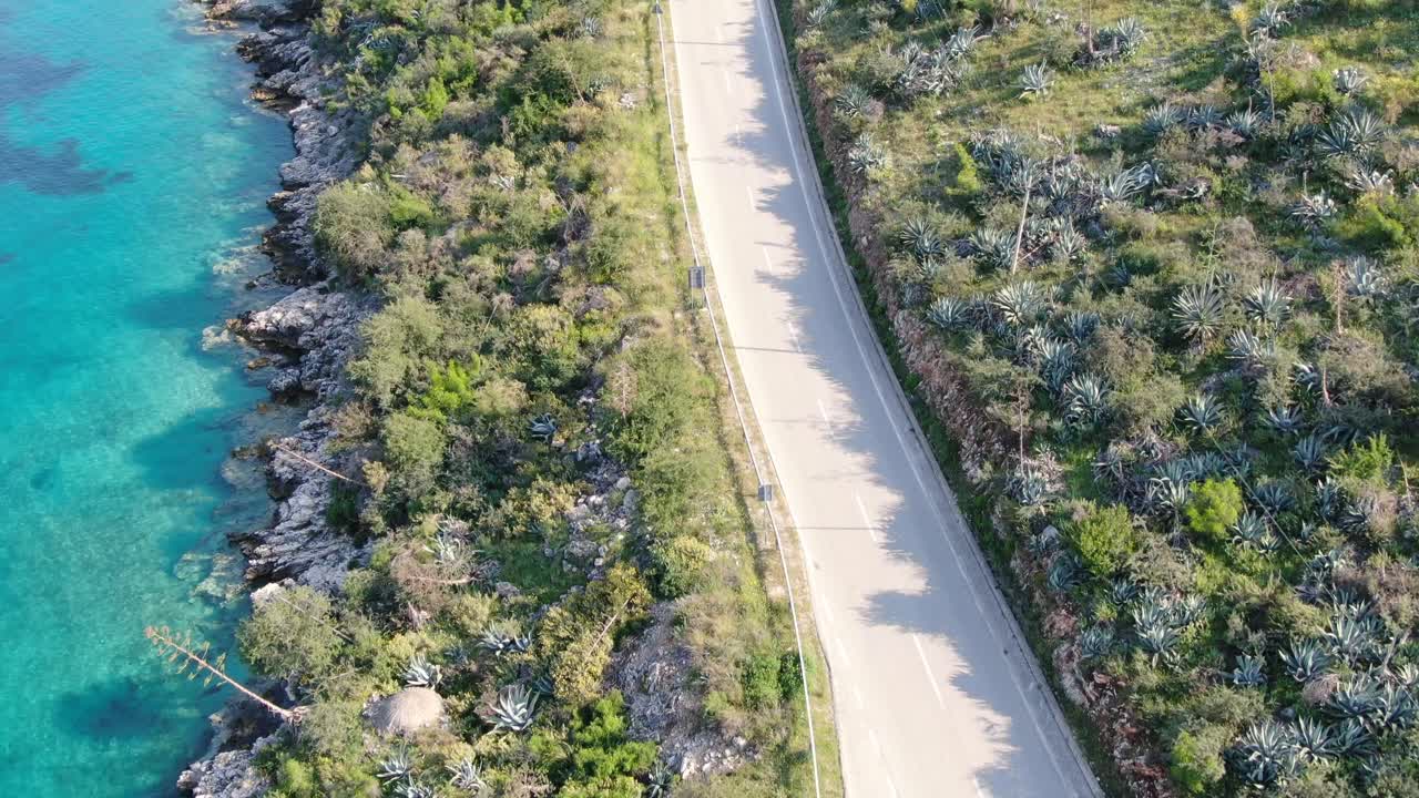 дронный вид в албании, летящий над дорогой с транспортными средствами, проезжающими мимо с чистым голубым океаном и зеленым ландшафтом по бокам