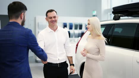 young married couple take congratulations from auto dealer, hugging each other