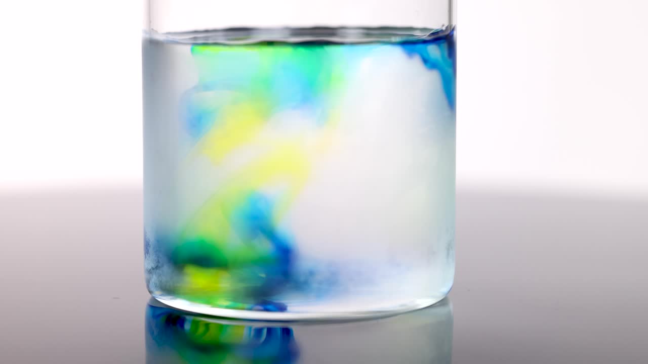 Blue and yellow dye swirl and diffuse in clear cold water, under bright studio lighting