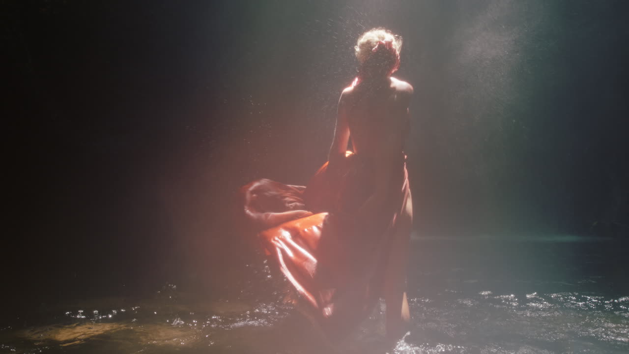bellissima donna che balla nella grotta della cascata indossa un bellissimo vestito si gode la danza sentendo la libertà spirituale 4k