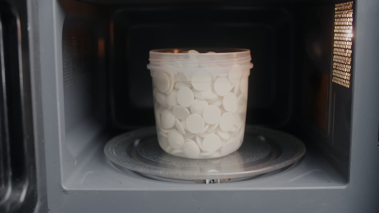 Hand in Gloves Placing a Container of White Chocolate Pieces in Microwave
