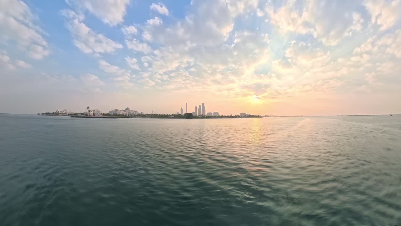 Abu Dhabi skyline in the United Arab Emirates at sunrise in this motion time lapse hyper lapse from a speedboat. Captivating sunrise colors paint the cityscape during a mesmerizing golden hour view