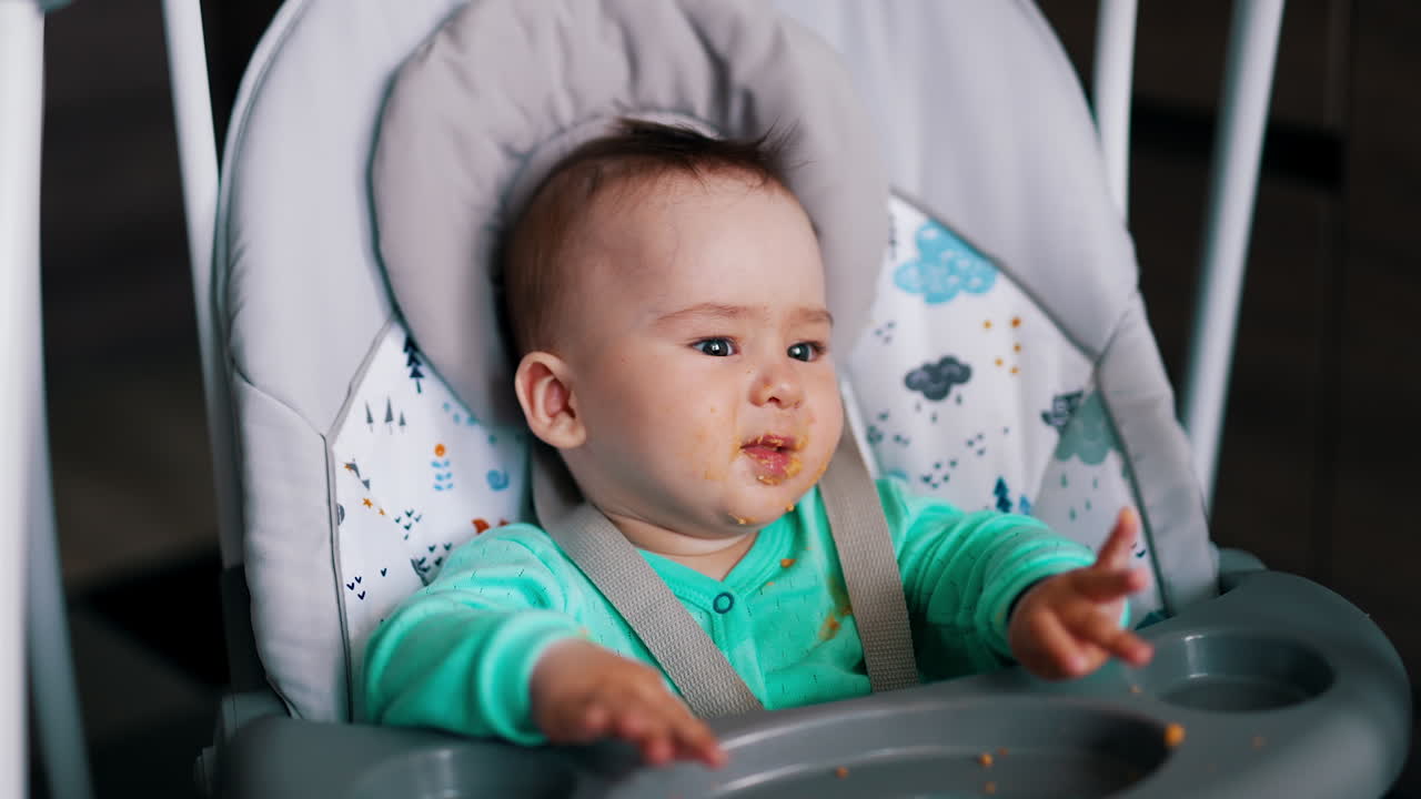 Active healthy Caucasian boy being fed from spoon. Cute child sits in a chair and waves his hands.