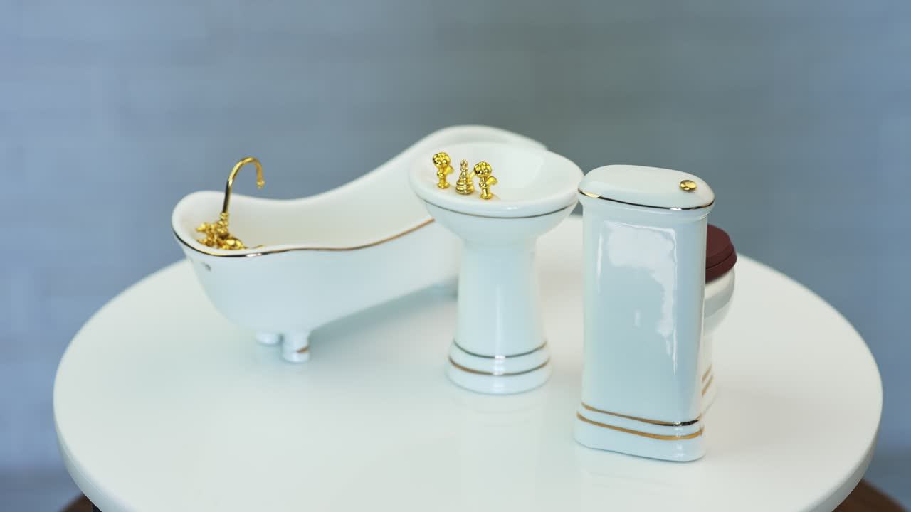 White plumbing for doll's house bathroom. Miniature sanitary engineering with golden appliances. Close up.