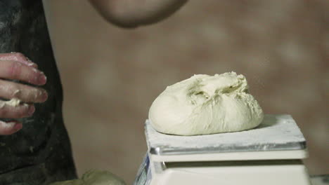 hands of a baker weighing the kneaded dough on a baking scale in the bakery