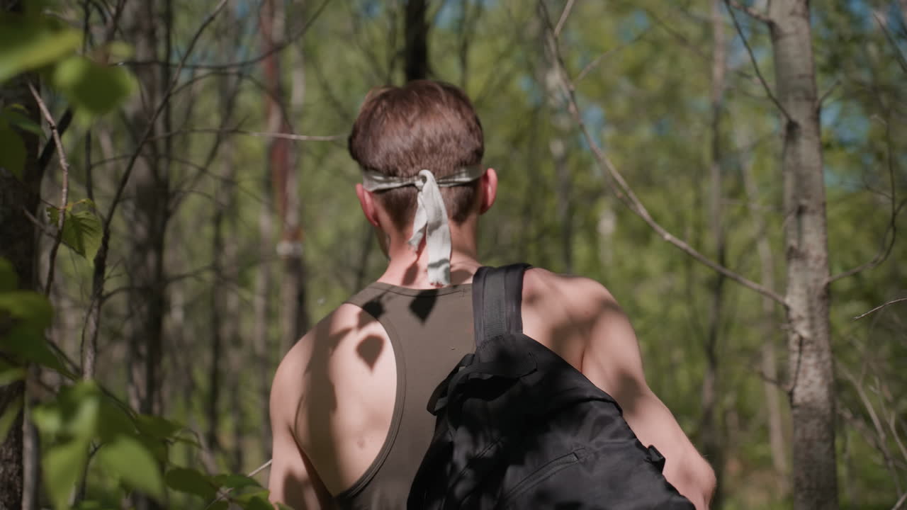 back view of adventurer walking through tall forest trees with sunlight highlighting fair skin headband backpack on shoulders capturing serene exploration under dappled green canopy