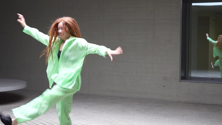 Woman in green suit dancing outdoors with mirror reflection showing energy elegance and joy