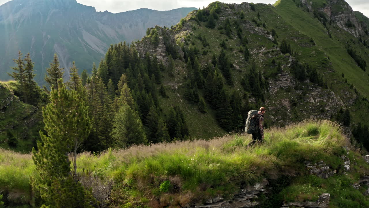 drone aéreo de tiro lateral siguiendo a un excursionista caminando por un sendero de montaña con mochila