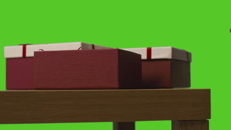 primer plano de un hombre poniendo un regalo en una caja envuelta en una mesa contra una pantalla verde