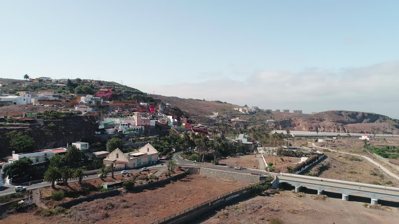 Vista aérea de un pueblo en la ladera de una colina con un puente y un paisaje árido.