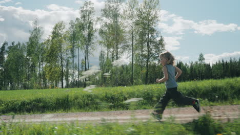 profile tracking shot of child running along country road between lush fields