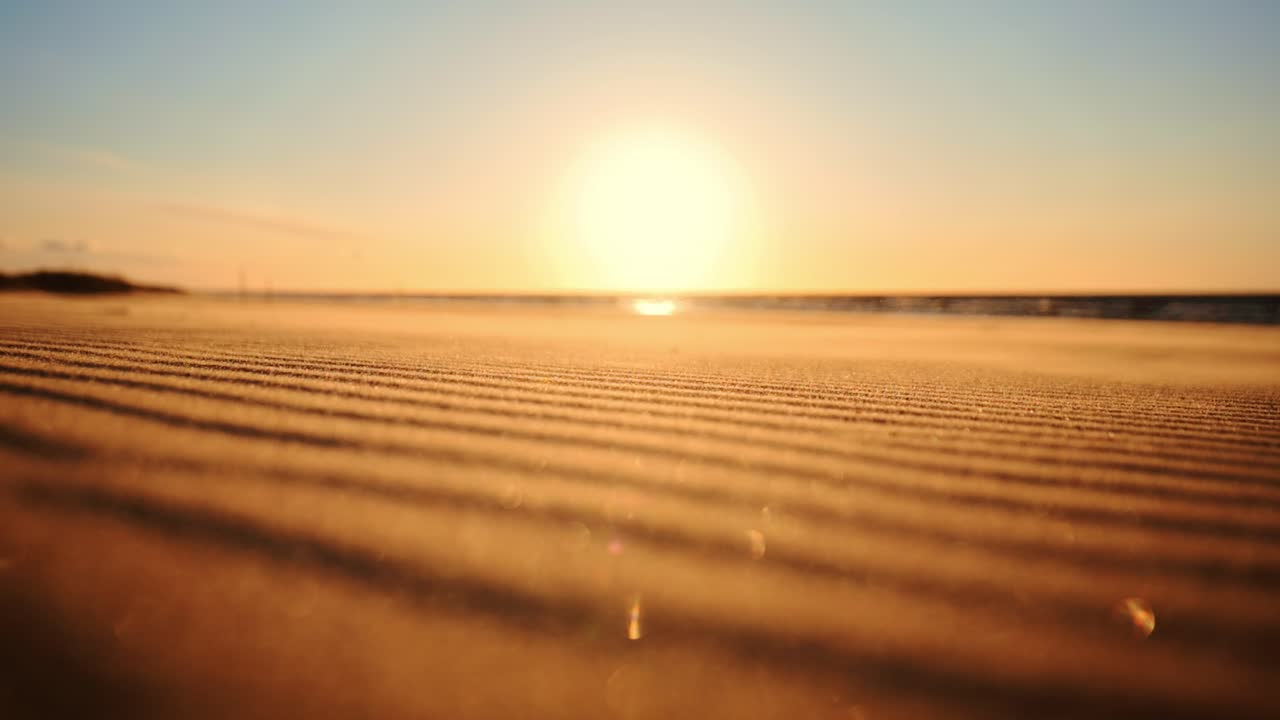 Waves of sand drift across coastal beach in golden glow of Oregon sunset