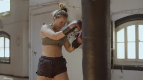 Plano-Medio-De-Una-Mujer-Exhausta-Pateando-Y-Golpeando-Un-Saco-De-Boxeo