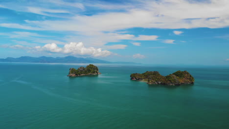 Drone-Volando-Lejos-De-Dos-Pequeñas-Islas-Montañosas,-Pulau-Gasing-Y-Pulau-Pasir,-Disparado-Desde-Una-Playa-En-Langkawi,-Malasia