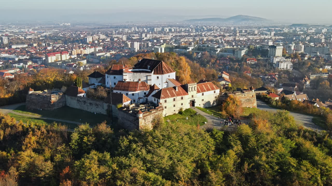 Aerial drone view of The Citadel in Brasov at sunrise, Romania. Medieval fortress on the top of a hill. Buildings, yellowed trees, tourists