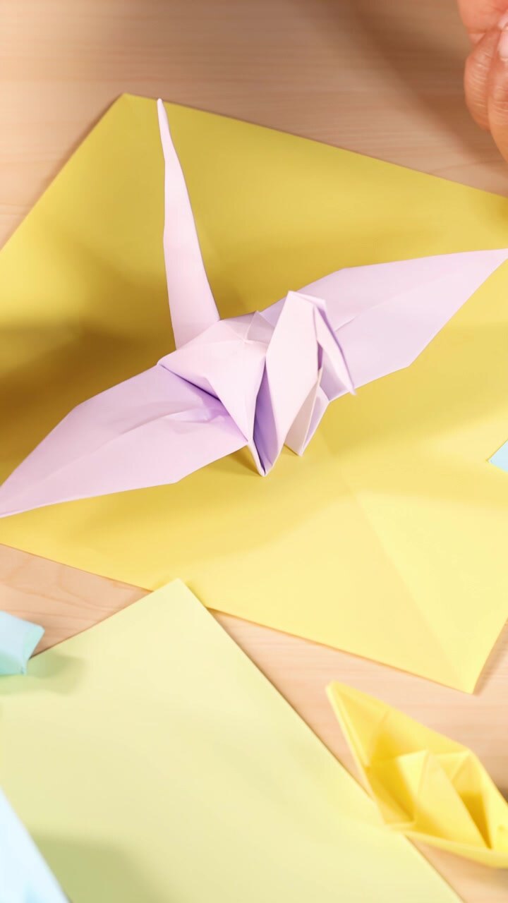 Una persona piega con cura carta pastello in una gru di origami, illuminazione brillante, angolazione della telecamera dall'alto