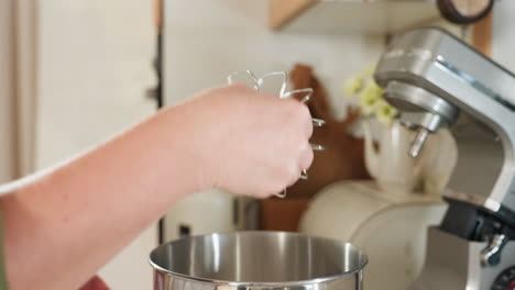 close up of chef hand lifting electric mixer attachment coated with thick flour mixture from stainless steel mixing bowl in cozy home kitchen