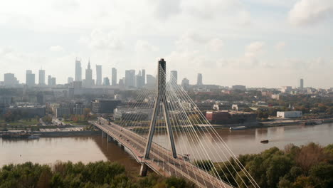 Slide-and-pan-shot-of-beautiful-modern-design-bridge-spanning-river.-Skyline-with-downtown-high-rise-office-buildings-in-background.-Warsaw,-Poland