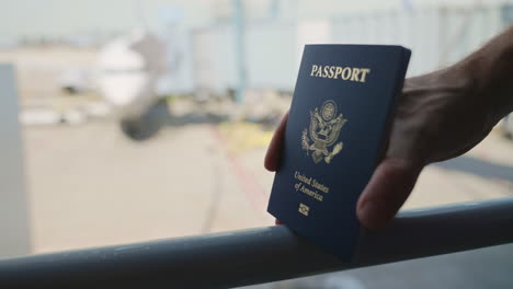 hands holding american passport while waiting to board international flight in airport terminal or gate