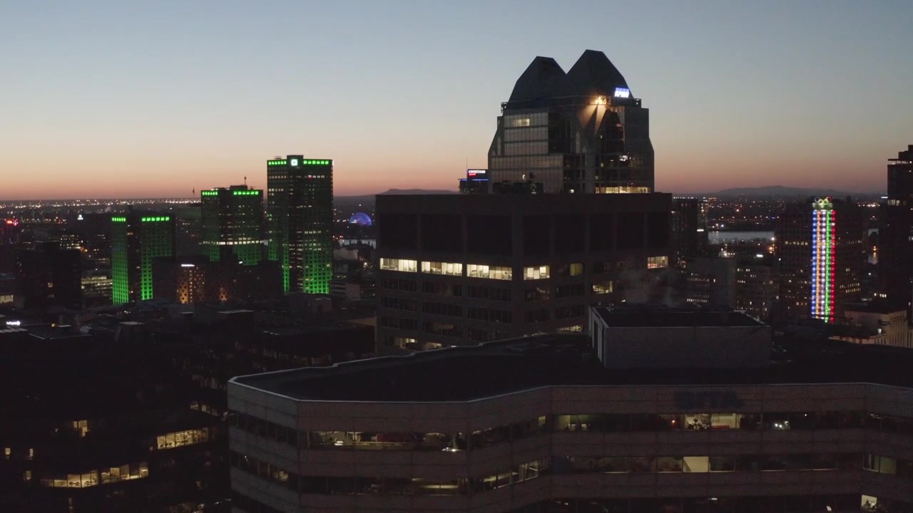 Le finestre a strisce di un grattacielo per uffici risplendono contro il cielo crepuscolare che svanisce mentre gli spazi di lavoro interni si illuminano attraverso lo skyline di Montreal
