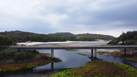 Traffic-driving-over-Morar-River-Bridge-near-Silver-Sands-Beach-in-Morar,-West-Coast-of-Scotland---Aerial-Drone-4K-HD-Fly-Towards