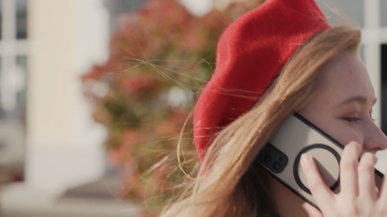 Hvid kvinde med kamera tjekker telefonen under en gadeoptagelse, hænderne på telefonen og kameraremmen, et fokuseret kreativt øjeblik med efterårslys, professionelt udstyr og et blidt smil midt i en samtale.