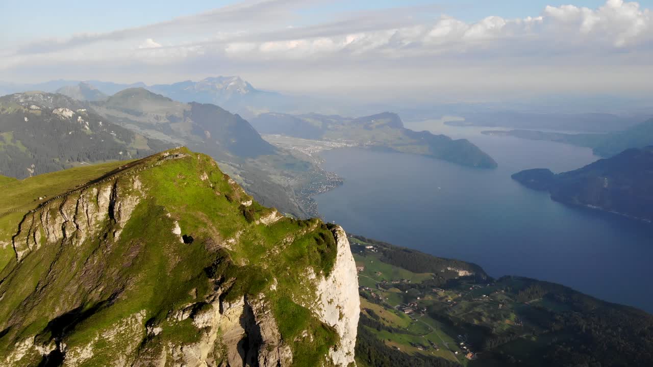 Aerial flyover towards Niederbauen Chulm in Uri, Switzerland with a view of cows grazing and mountain peak's tall cliffs above Lake Lucerne on a summer morning in the Swiss Alps