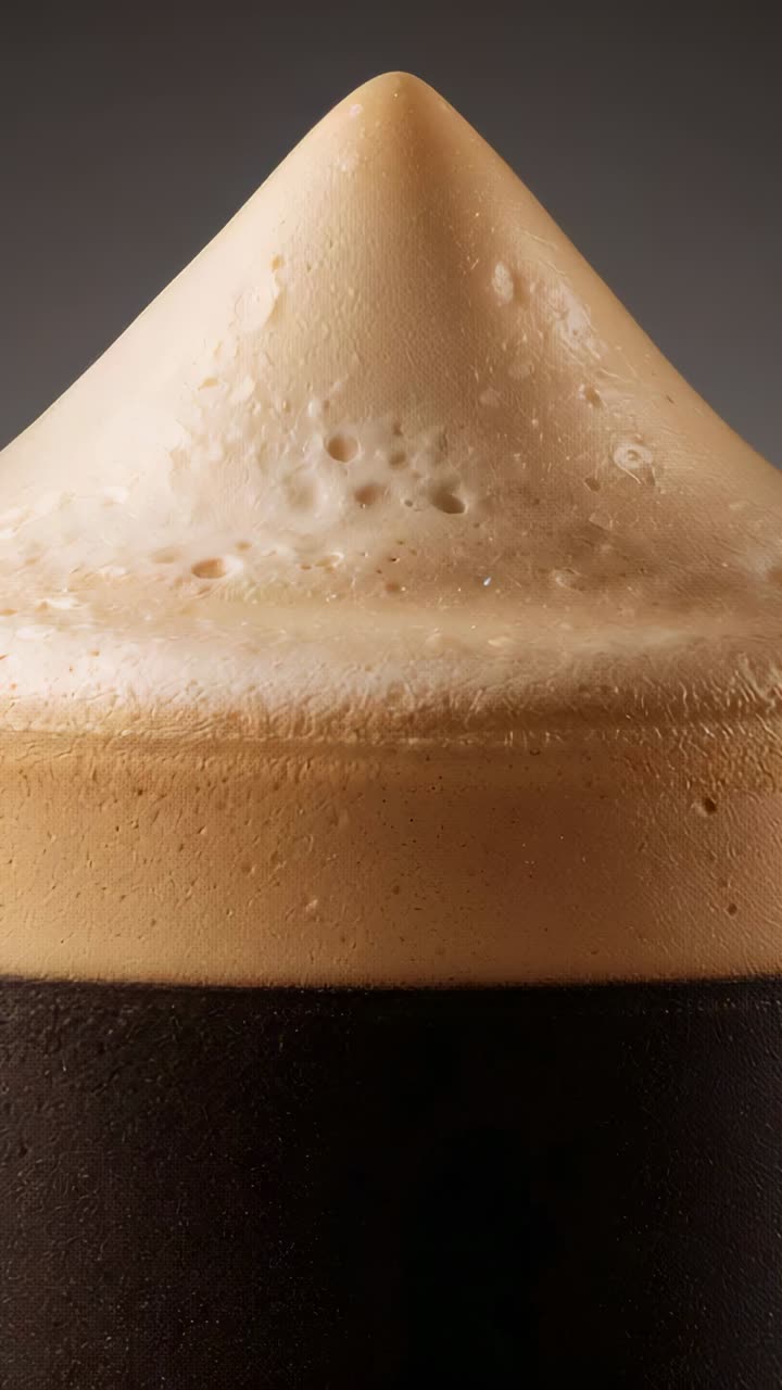 Video verticale: ripresa di un bicchiere alto di birra scura che mostra la schiuma che si deposita in studio, evidenziandone la texture