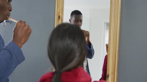 video of happy diverse couple brushing teeth looking in mirror in bathroom at home