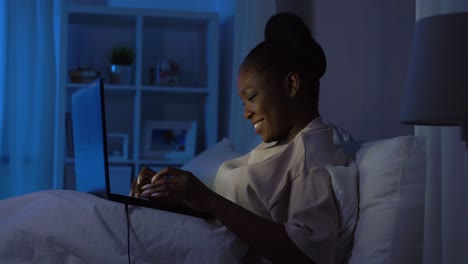 African-Woman-with-Laptop-in-Bed-at-Home-at-Night.technology,-internet,-communication-and-people-concept-young-african-american-woman-with-laptop-computer-lying-in-bed-at-home-at-night