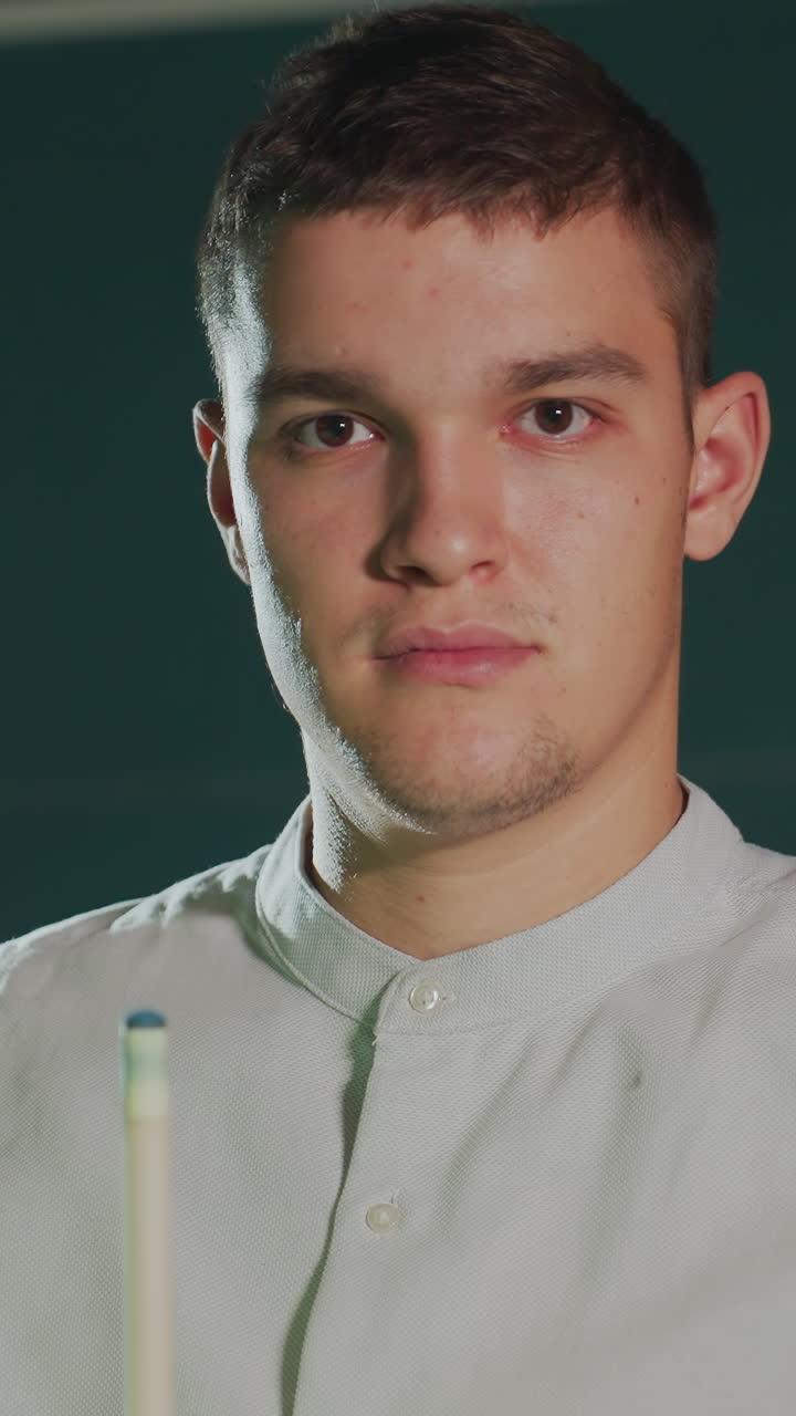 tipo con rostro serio vestido con camisa blanca contra un fondo oscuro sosteniendo cuidadosamente el palo de la clave, aplicando la cubierta roja con expresión enfocada. la iluminación destaca la concentración, la precisión